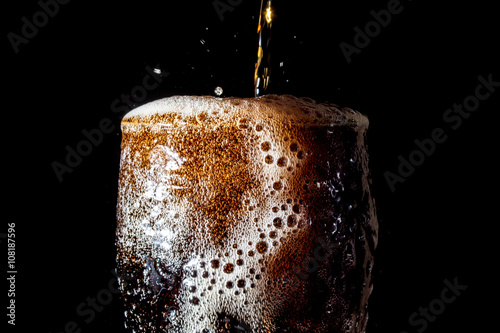 Soda large glass, overflowing glass of soda closeup with bubbles isolated on black background
