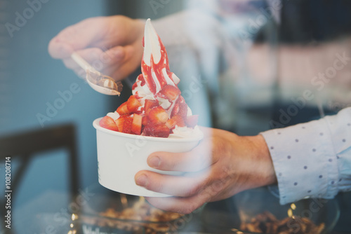seller pours sauce on a soft frozen yogurt in white take away cup