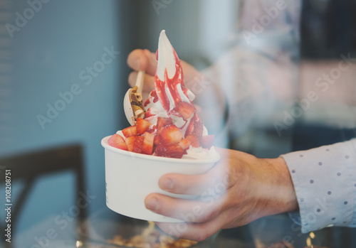 seller pours sauce on a soft frozen yogurt in white take away cup