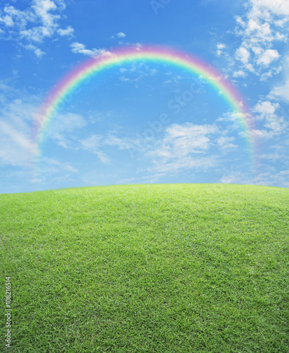 Rainbow with green grass field over blue sky, nature background