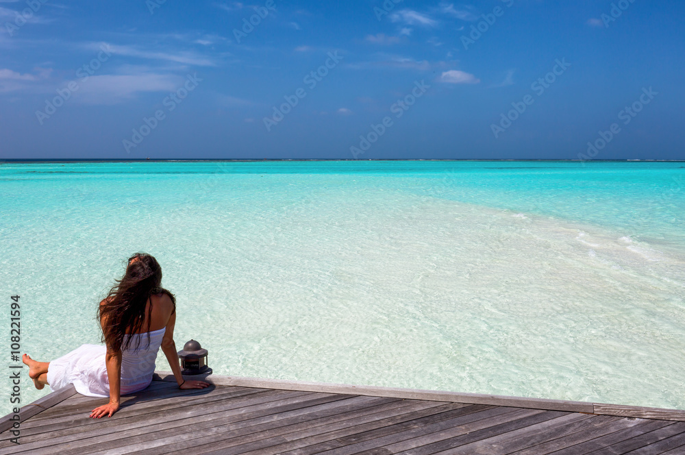 Frau sitzt auf einem Holzsteg auf den Malediven