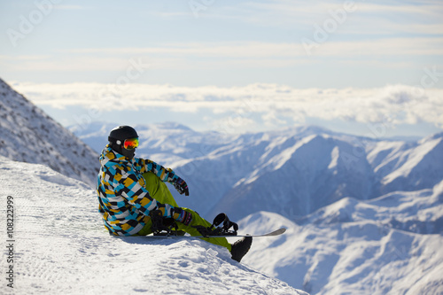 Snowboarder looking at mountains sitting on mountain top
