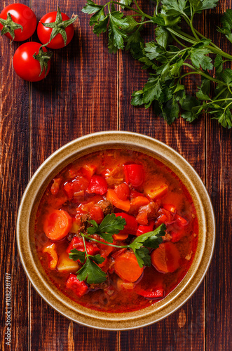 Goulash or stew in bowl served with parsley on wooden background