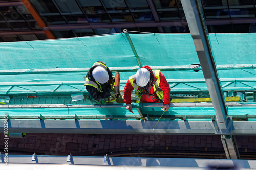 two workers on construction site. Two construction workers working on a platform and measuring flashings. Safety concept on construction site - Hard hats workers with the tools - Focus on helmets.