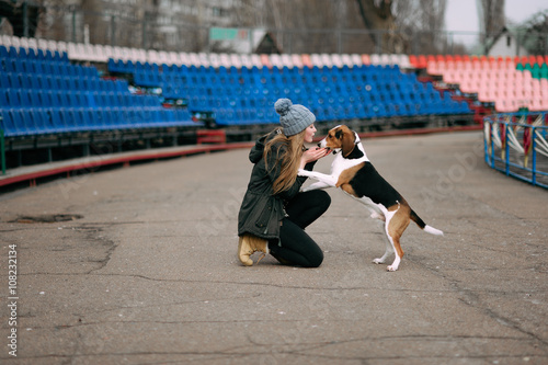 Young hipster girl with her pet estonian hound dog playing, junping and hugging and having fun outdoor at the old stadium.