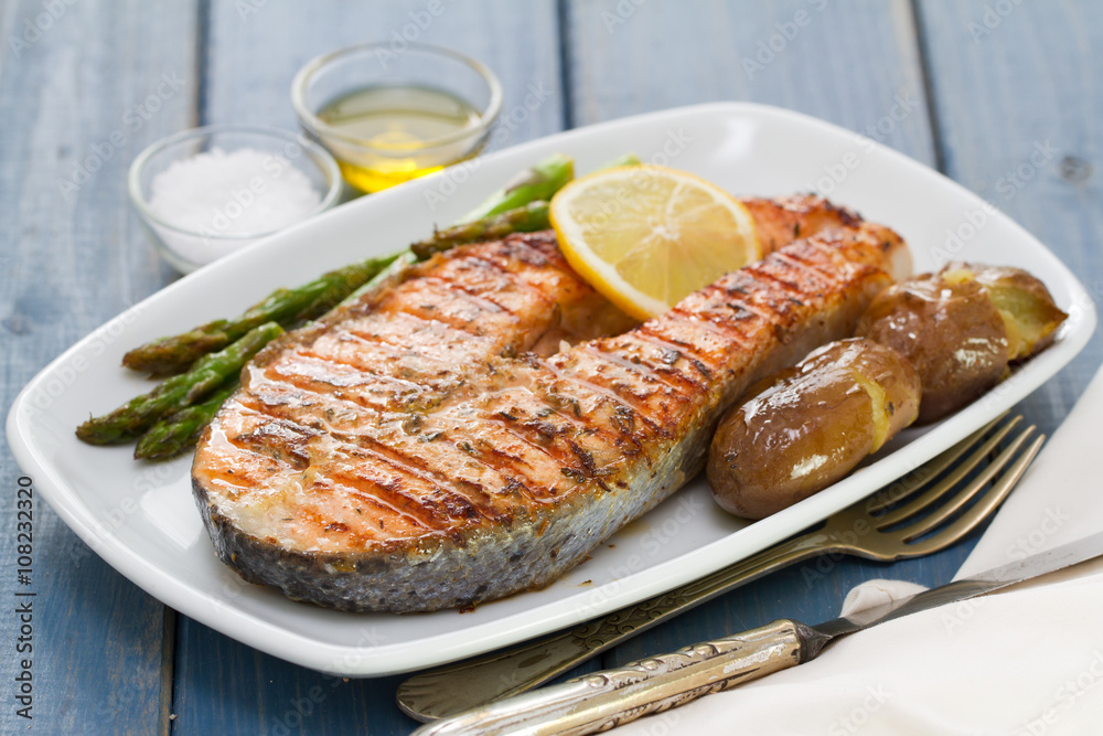 grilled salmon asparagus and potato on white dish on blue wooden background