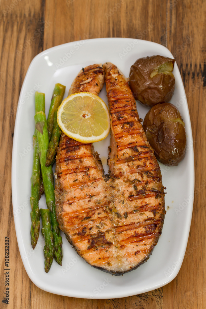 grilled salmon asparagus and potato on white dish on brown wooden background