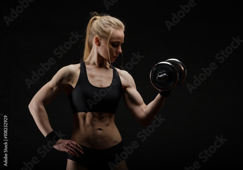 Young slim strong muscular woman posing in studio with dumbbell