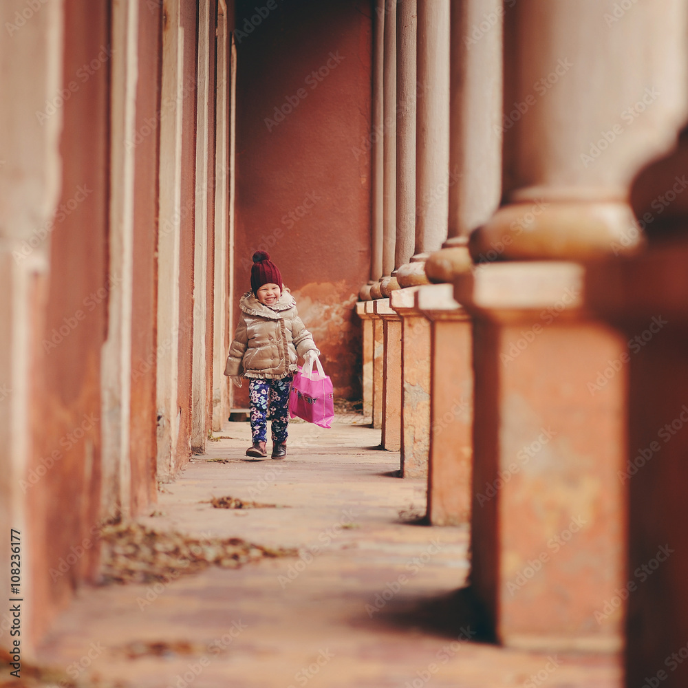 Маленькая девочка в теплой куртке и шапке бежит по коридору