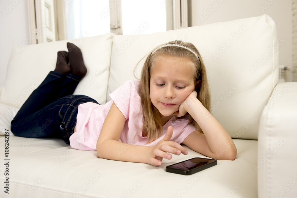 happy blond little girl on home sofa using internet app on mobile phone happy blond little girl on home sofa using internet app on mobile phone
