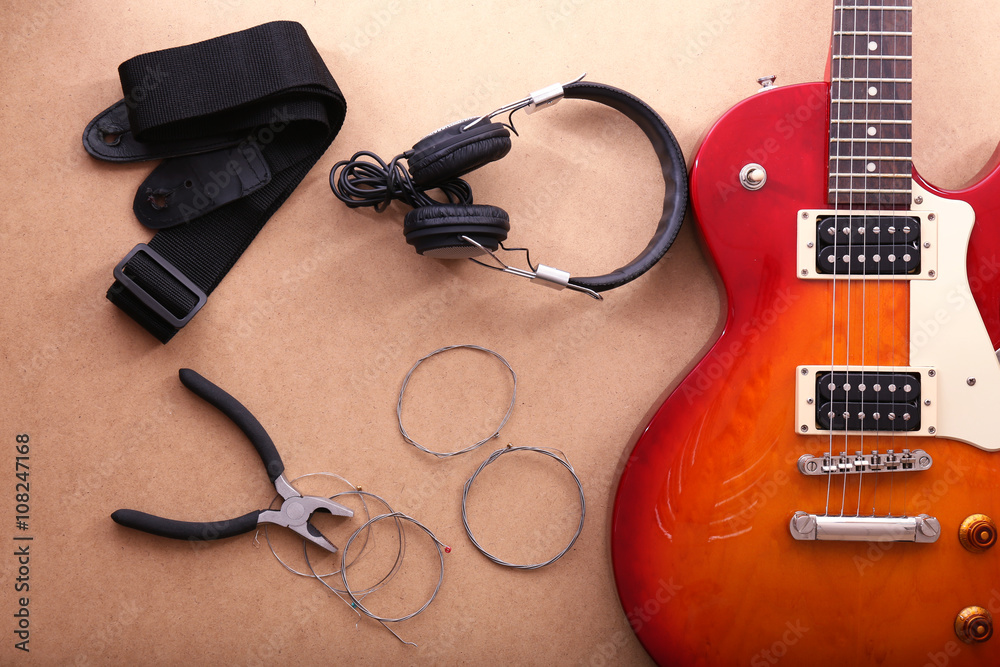 Naklejka premium Electric guitar with headphones, pliers and strings on beige background