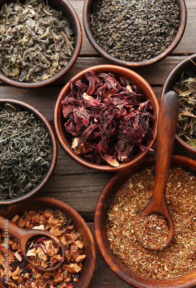 Variety of tea in round bowls with spoon on wooden table, top view Variety of tea in round bowls with spoon on wooden table, top view