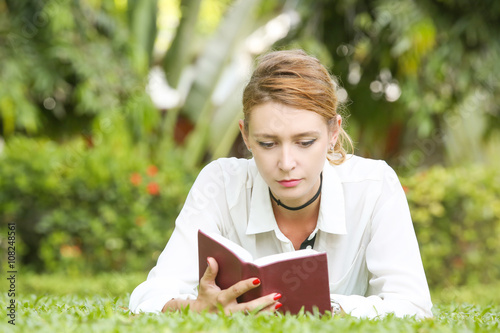 A portrait of a young woman reading a book in the park