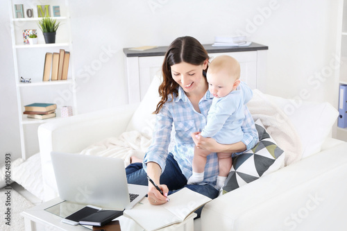 Beautiful woman with baby boy working from home using laptop