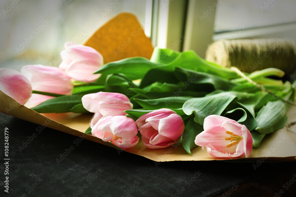 Bouquet of pink tulips on wrapping paper over black wooden windowsill Bouquet of pink tulips on wrapping paper over black wooden windowsill