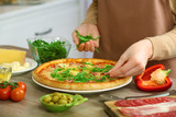 Woman decorating fresh baked pizza with arugula, close up