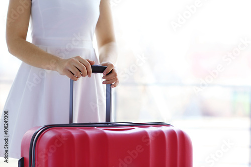 Woman in white dress holding a large red suitcase, close up © Africa Studio