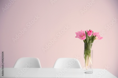 Beautiful tulips on dinning table against white wall background