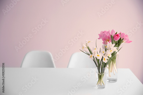 Beautiful tulips and irises on dinning table against white wall background