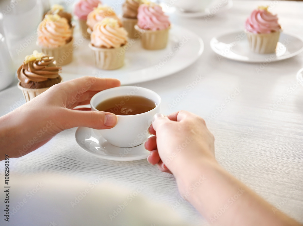 Female hands at the table with tea and cupcakes closeup Female hands at the table with tea and cupcakes closeup