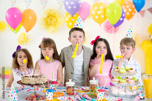 Happy group of children with yellow noise makers having fun at birthday party