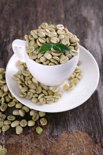 Green coffee beans in a white cup on wooden table