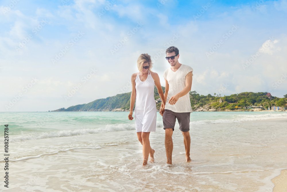 Beautiful young couple walking along the shore of a tropical sea Beautiful young couple walking along the shore of a tropical sea