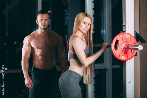 Young couple exercising in gym with weights  man seems to be the personal trainer