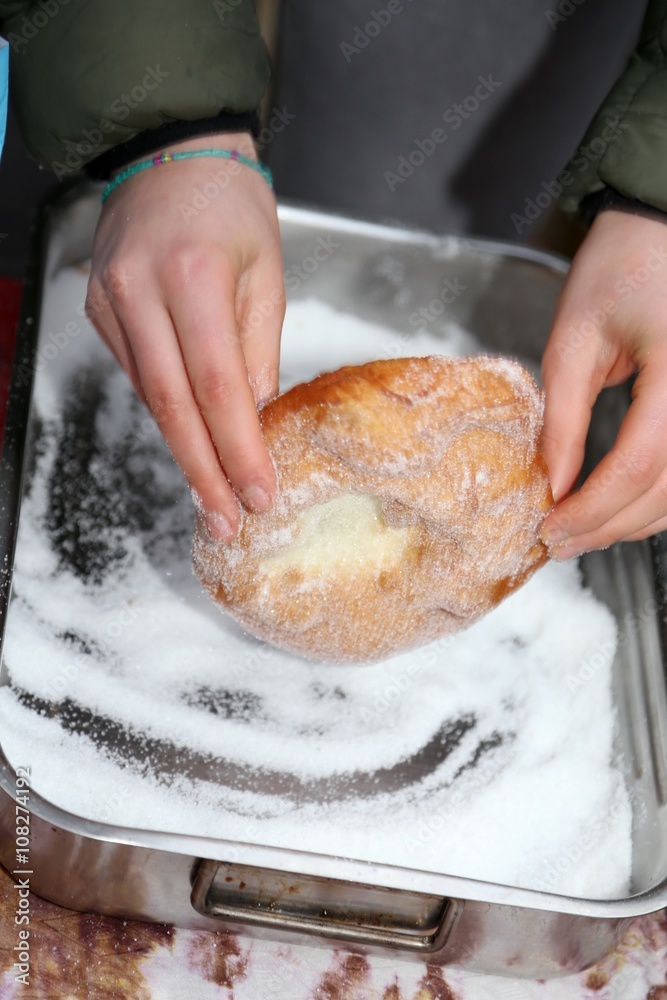 hands of young street vendor while spreading sugar on fried hot
