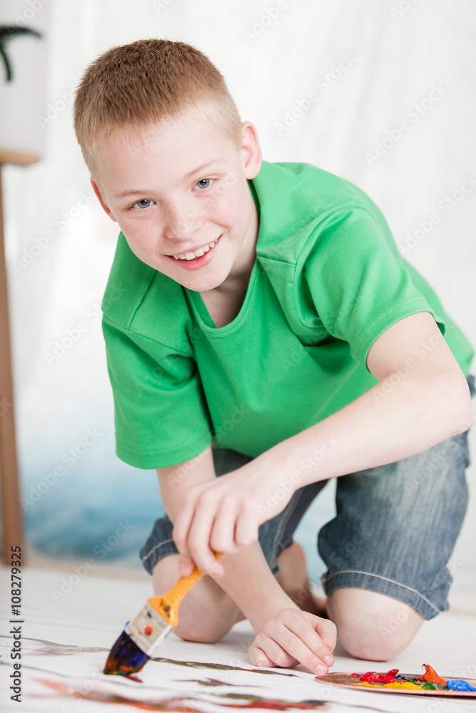 Boy kneeling on painting while holding brush Boy kneeling on painting while holding brush