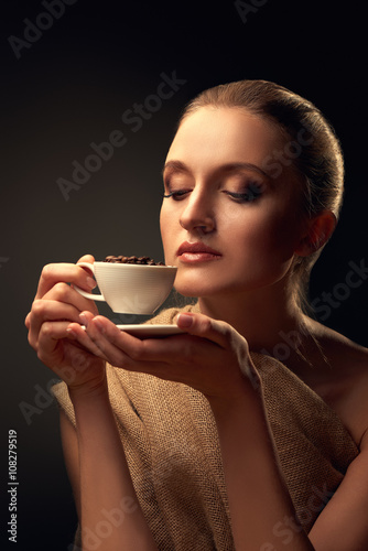 Tender beautiful woman holding coffee cup and beans over dark gradient background