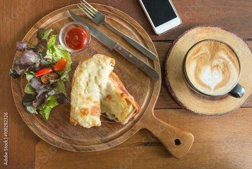 Bread baked with cheese and ham , vegetable , tomato sauce on wooden plate served with latte hot coffee. Set of homemade breakfast.