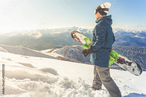 Adventure to winter sport. Snowboarder man hiking at mountain photo