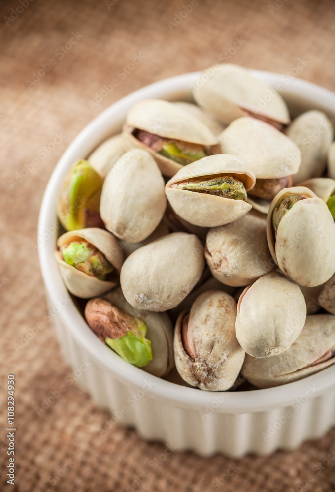 Pistachios in white ceramic jar on rustic fabric background Pistachios in white ceramic jar on rustic fabric background