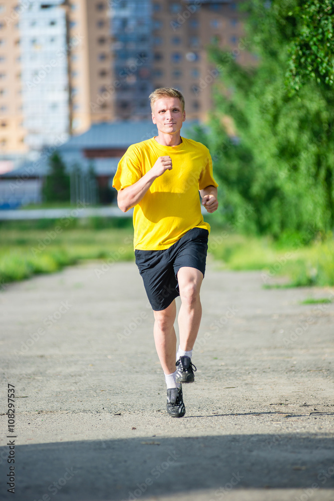 Running man jogging in city street park at beautiful summer day. Sport fitness model caucasian ethnicity training outdoor.