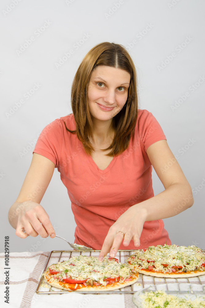The girl at the table puts toppings on a pizza with a satisfied look on his face