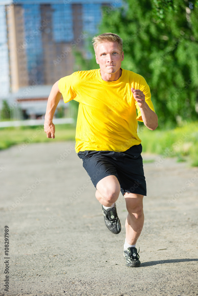 Running man jogging in city street park at beautiful summer day. Sport fitness model caucasian ethnicity training outdoor.