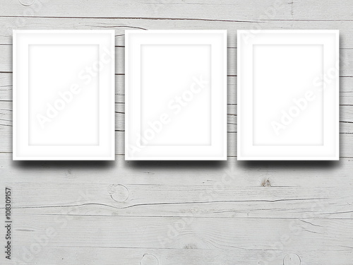 Close-up of three blank white picture frames on light grey wooden background