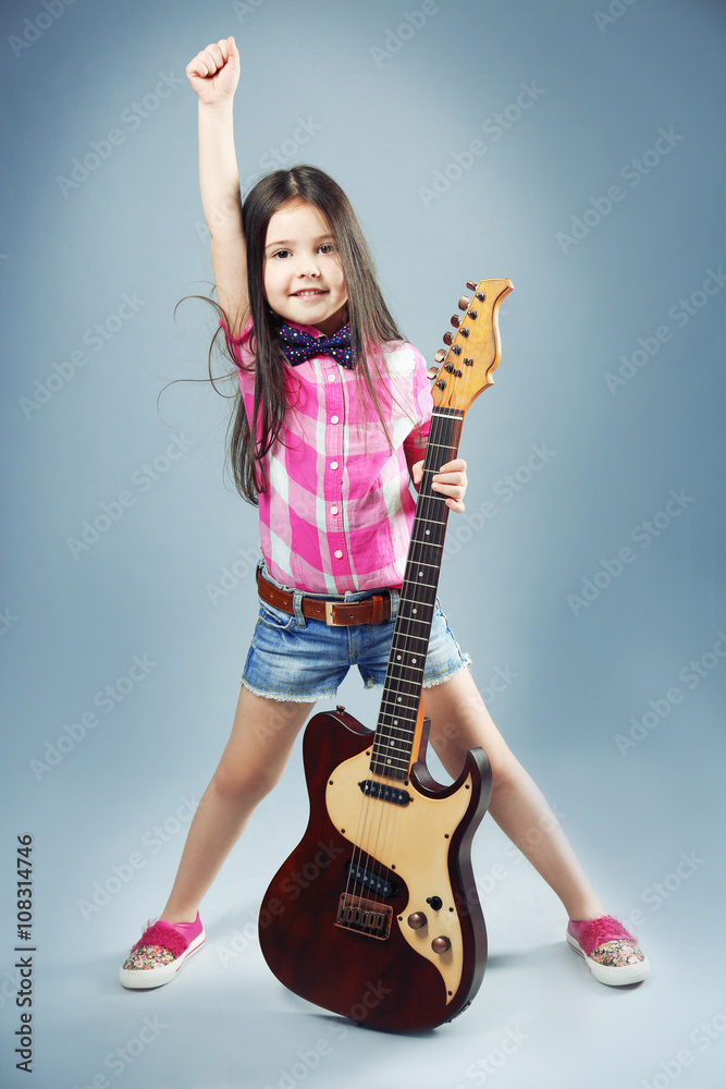 Beautiful artistic little girl playing guitar on grey background Beautiful artistic little girl playing guitar on grey background