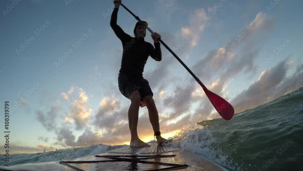 Stand up paddle board surfing a wave at sunset
