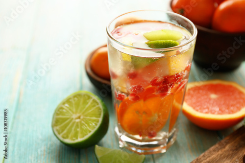 Refreshing cocktail with ice, mint, pomegranate seeds and slices of fruits on blue wooden background