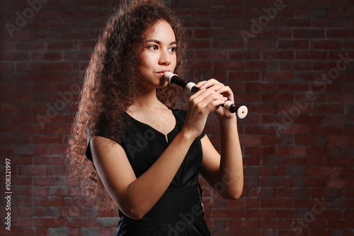 Photos Beautiful young woman playing on recorder over brick wall background