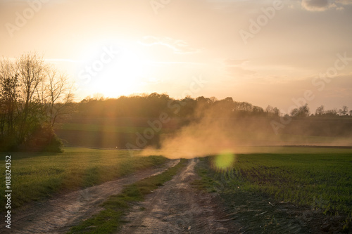 Country road landscape in sunset. Sun rays through the dust.