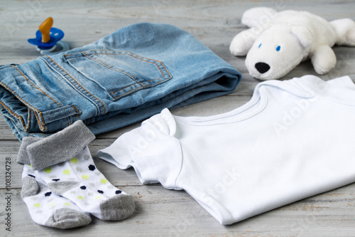 Baby clothes and accessories with white bear toy on a wooden background