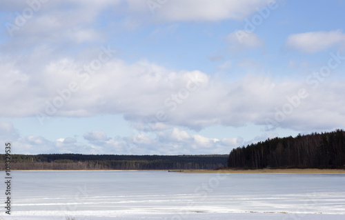 Frozen lake and cloudy sky. The lake is covered with ice in the woods. 