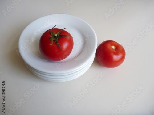 red tomato on a stock of white plates © luciezr