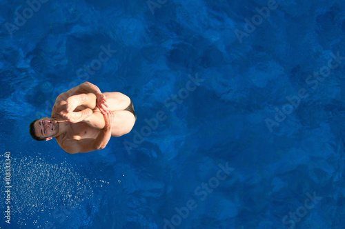 High diving athlete caught in the air above water surface. Shot from above