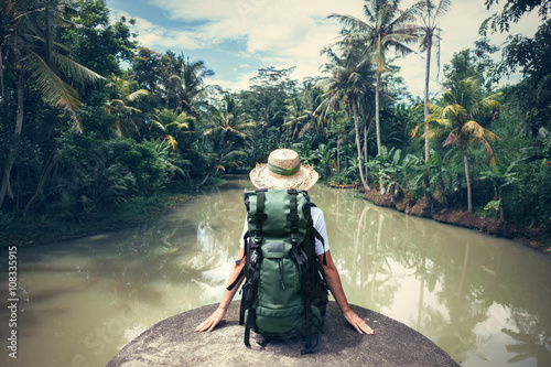 Woman traveler with backpack sitting on the edge and looking at tropical river (intentional vintage color) photo