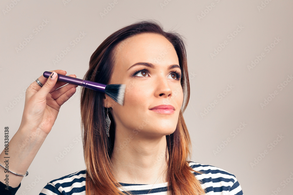 Obraz premium Makeup artist applying liquid tonal foundation on the face of the woman. Beauty Girl with Makeup Brush. Natural Make-up for Brunette. 