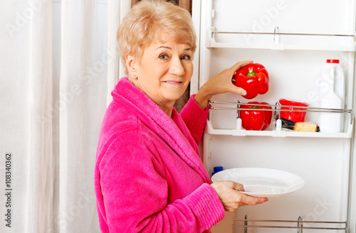 Senior woman taking a red paprika from fridge